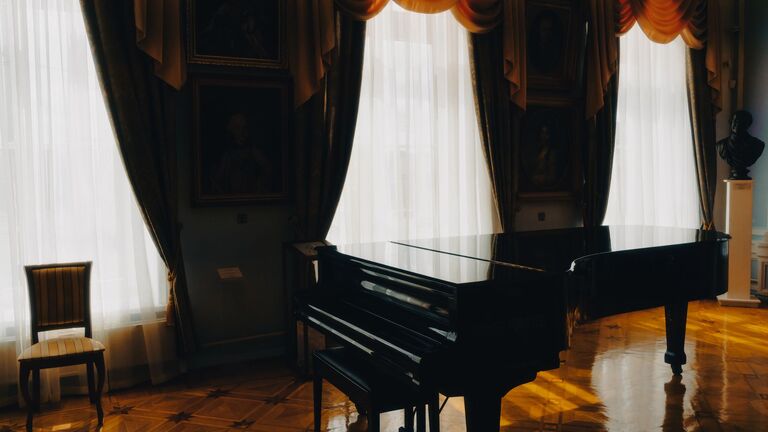 Piano de cola negro en un salón clásico con suelo de parqué y grandes ventanales con cortinas