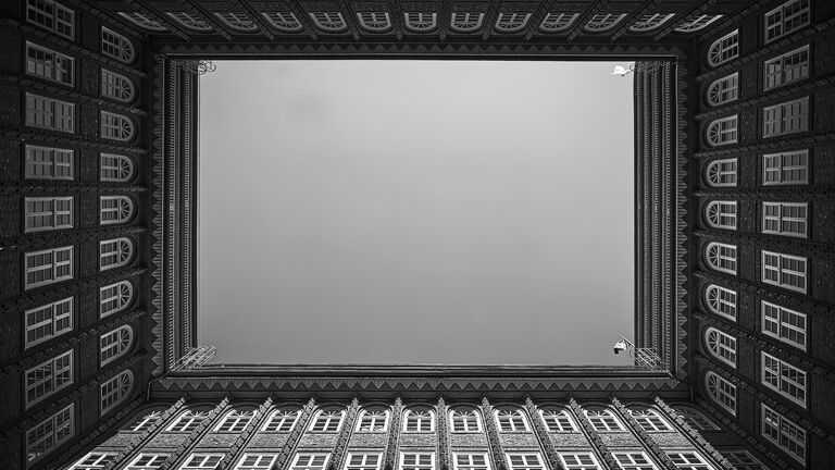 Patio interior de un edificio de viviendas visto desde abajo, con filas de ventanas en sus cuatro fachadas