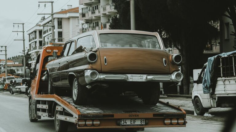 Coche clásico sujeto sobre la plataforma de un camión portavehículos en una calle con bloques de viviendas